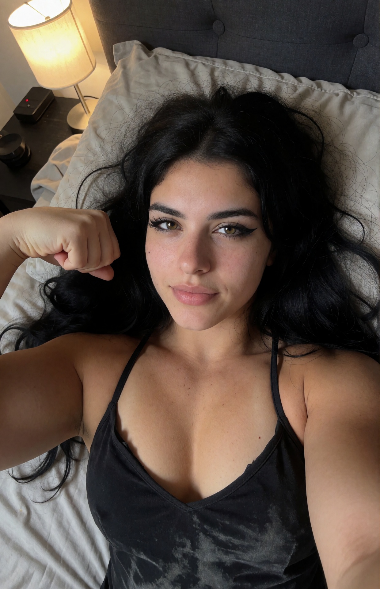 Your favorite goth muscle mommy takes a close-up overhead portrait selfie while lying comfortably across an unmade bed,  t...