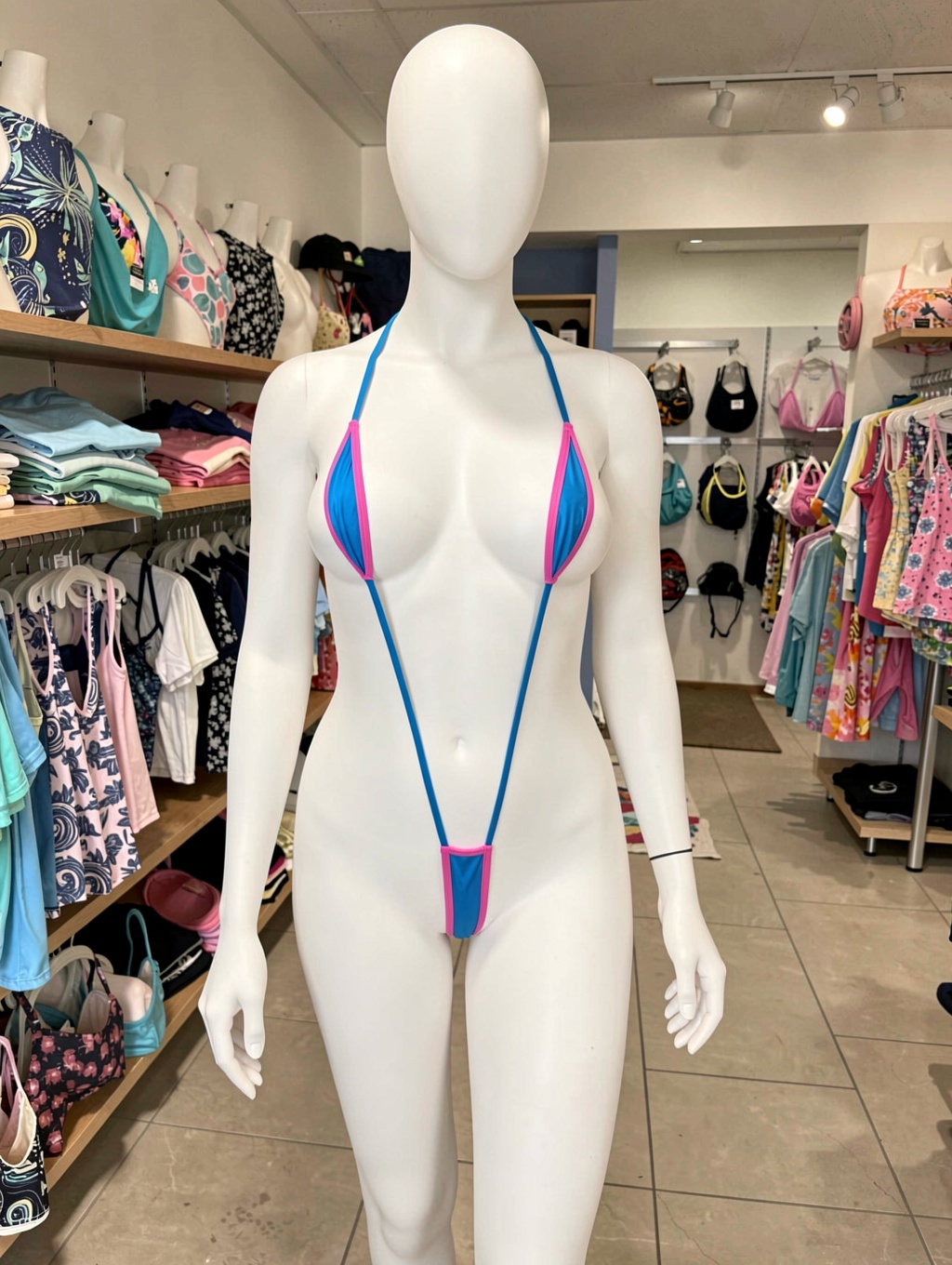A white female mannequin wearing an extremely small,  blue/pink monokini-style slingshot swimsuit; the mannequin is in a s...