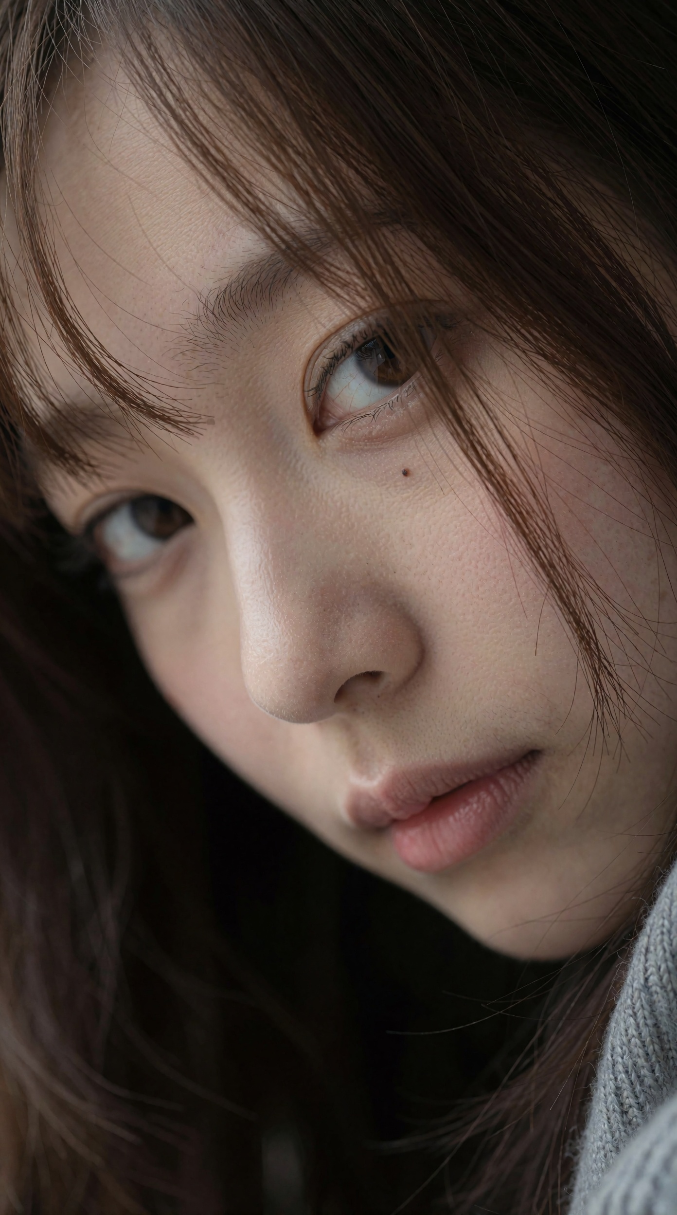 特写照片捕捉到一位年轻日本女子的脸微微向下倾斜,  她棕色的大眼睛以柔和的力度直视着观众,  淡棕色的细发部分遮住了她的脸 on Tensor.Art