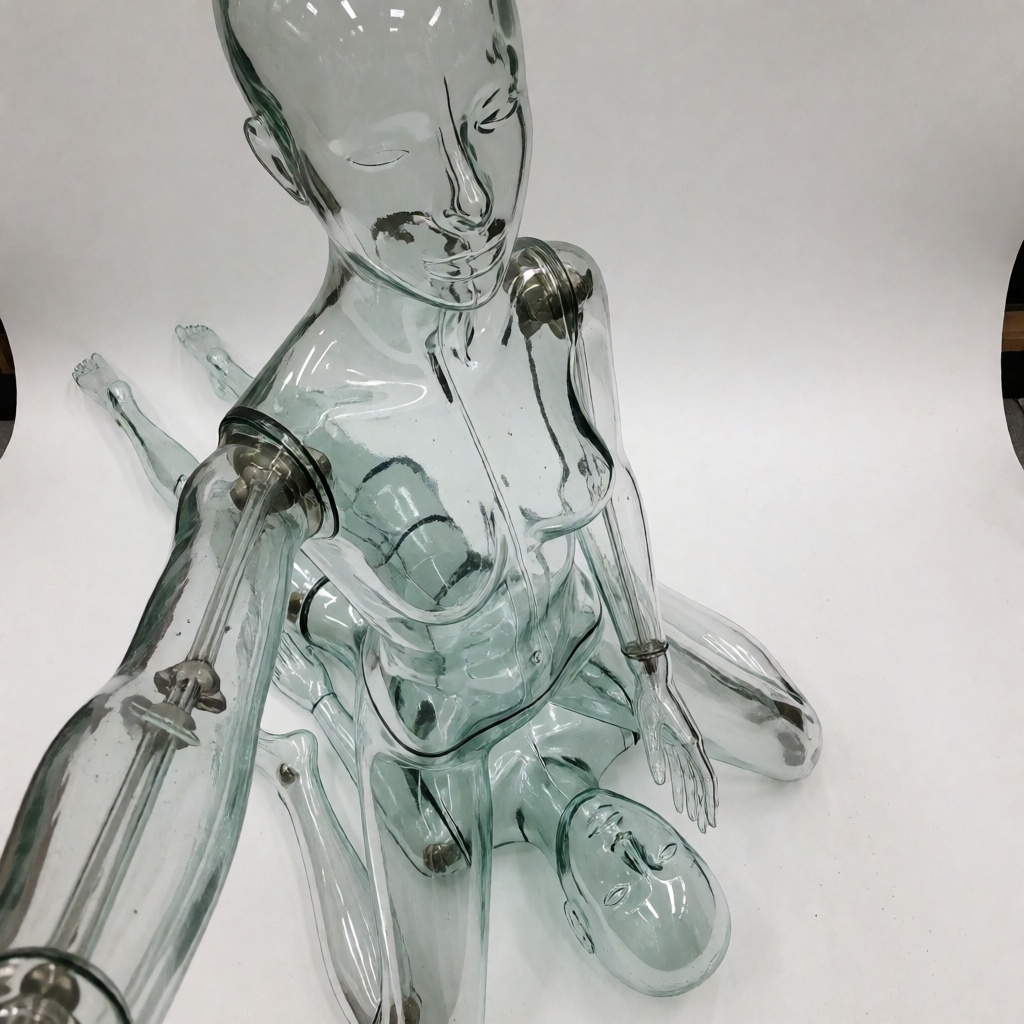 a glass mannequin is sitting over a jelly mannequin face,  the jelly mannequin is lying on it back under the glass mannequ...