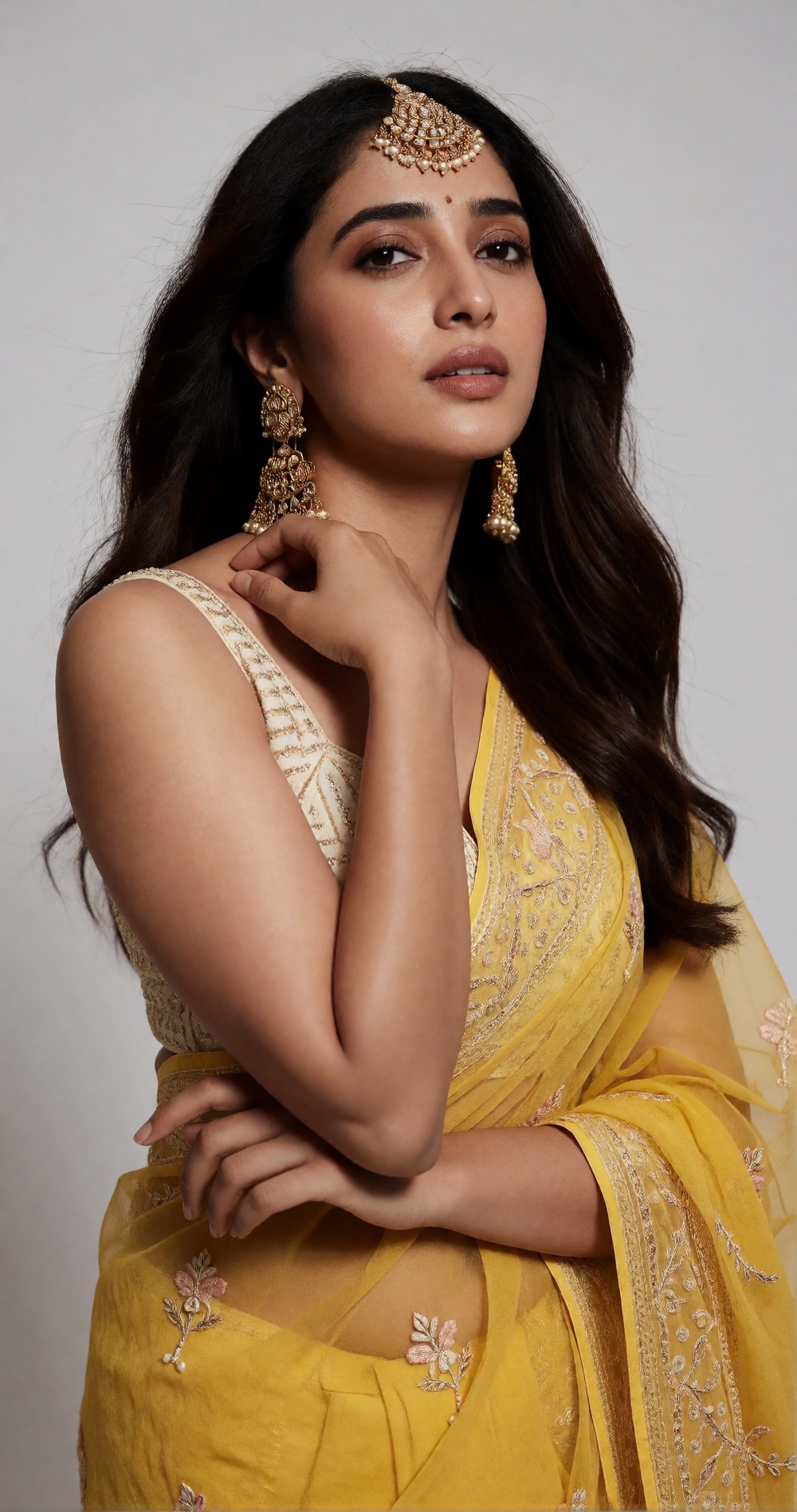 Photograph of a young South Asian woman with medium brown skin and long,  wavy dark brown hair. She is wearing a yellow sa...