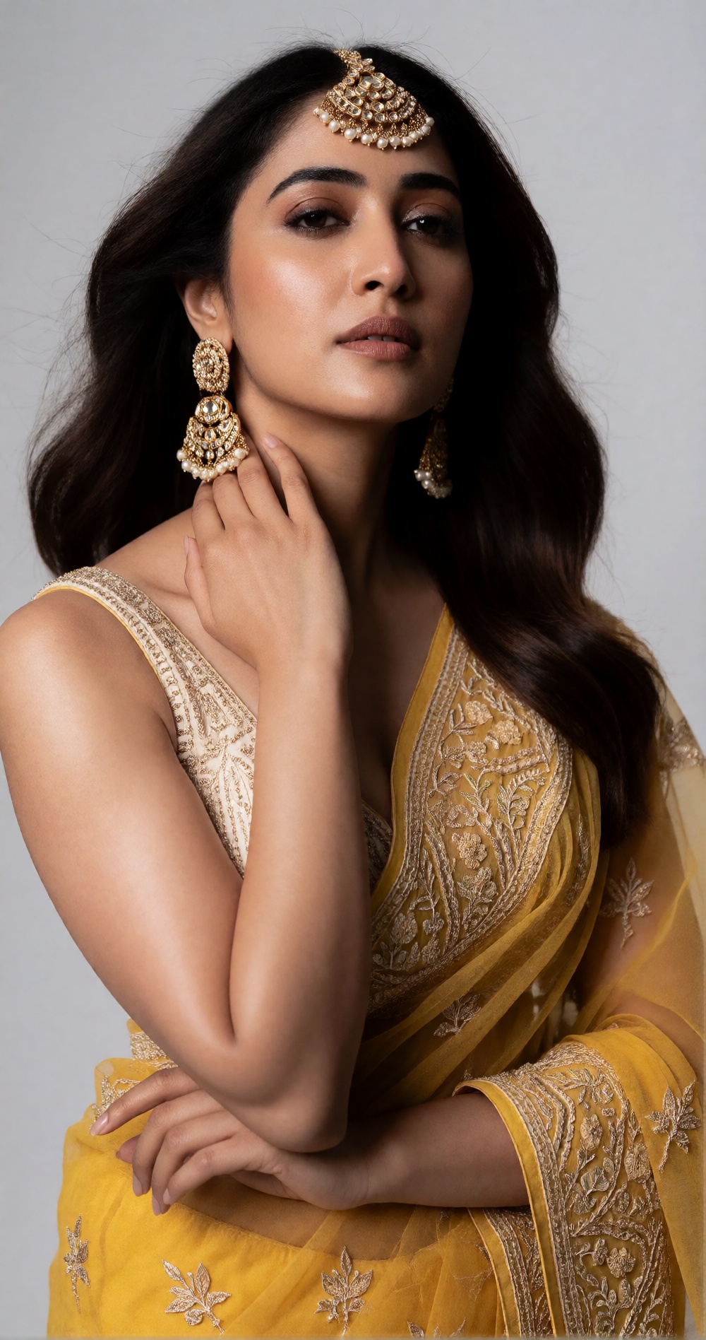 Photograph of a young South Asian woman with medium brown skin and long,  wavy dark brown hair. She is wearing a yellow sa...