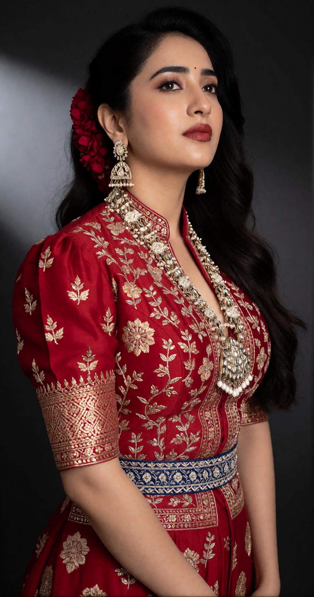 Photograph of a young South Asian woman with long,  wavy black hair adorned with a red floral hairpiece. She has a fair to...