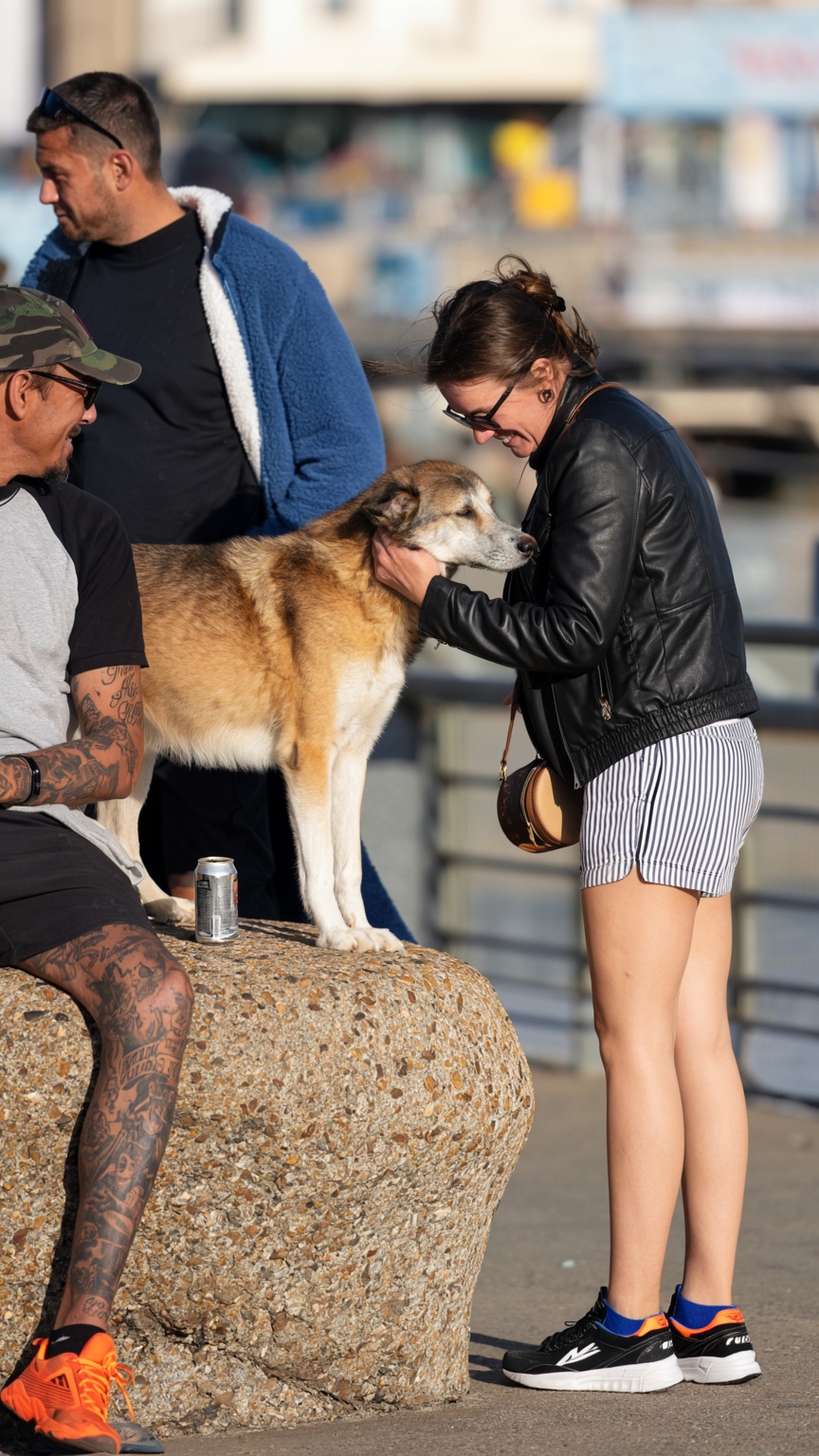 a large,  tan and white dog with a thick coat stands on a textured concrete boulder,  its head gently held by a woman in a...