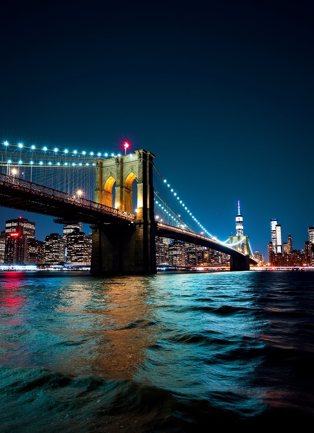 This is a stunning nighttime photograph capturing the Brooklyn Bridge from a vantage point on the water,  likely from a bo...