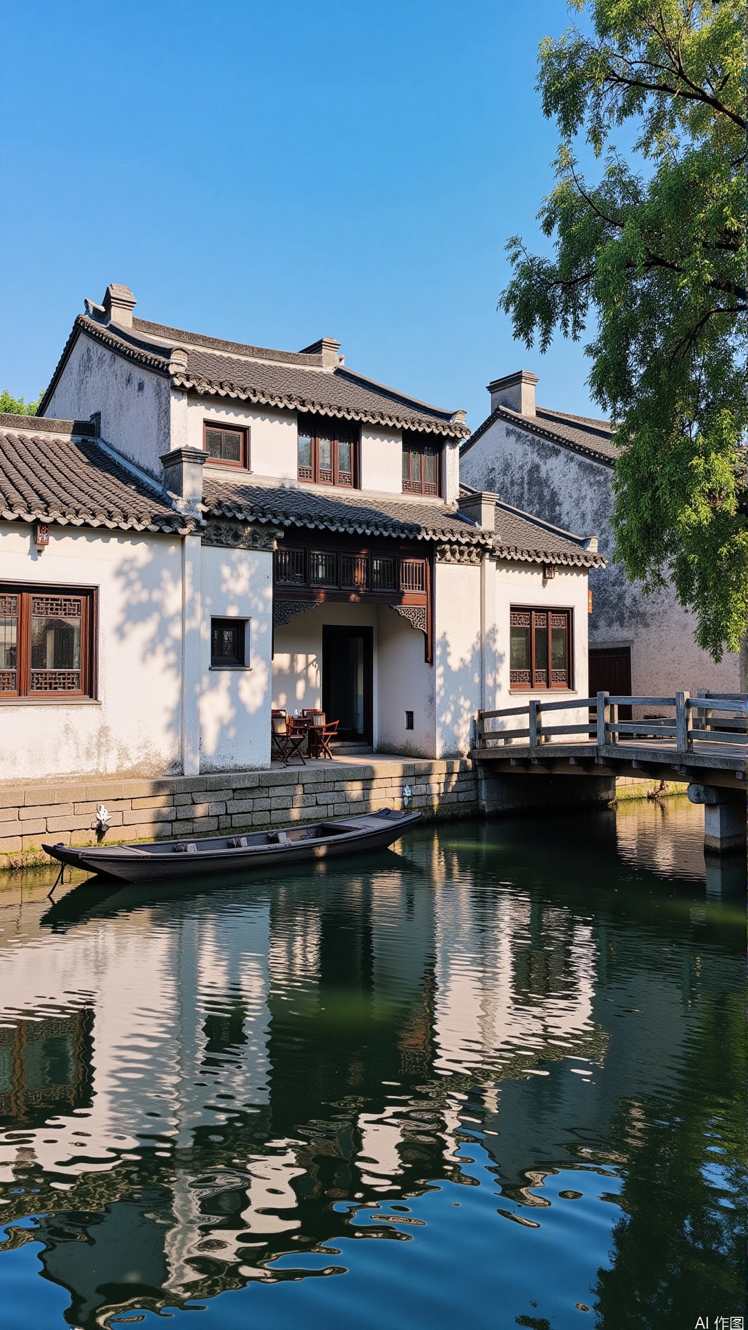 The image shows a traditional Chinese house with a small boat on a canal. The house is made of stone and has a white exterior with a black tiled roof. It has multiple windows and a balcony on the second floor. The canal is calm and there is a wooden bridge crossing over it. The sky is blue and there are trees in the background. The overall atmosphere of the image is peaceful and serene.