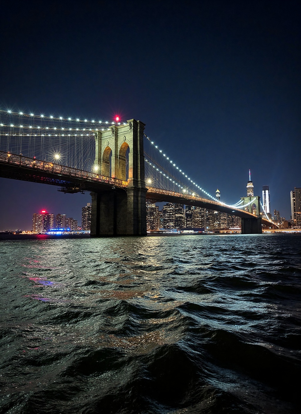 This is a stunning nighttime photograph capturing the Brooklyn Bridge from a vantage point on the water,  likely from a bo...