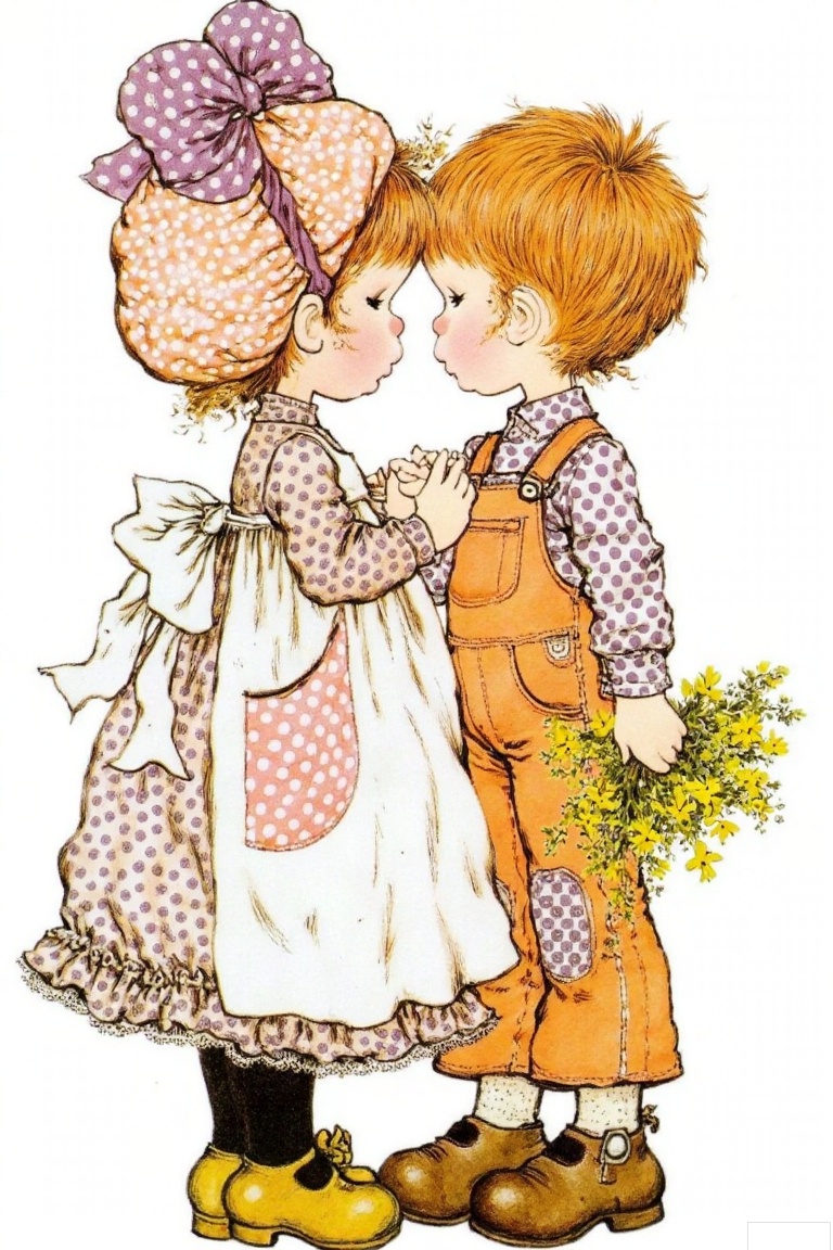 The image depicts two children standing close together. The child on the left is wearing a long-sleeved dress with a polka dot pattern and a large bow on their head. They are also wearing black tights and yellow shoes. The child on the right is dressed in orange overalls with a polka dot pattern on the shirt underneath. They have short red hair and are holding a small bouquet of yellow flowers. The background is plain white, emphasizing the children and their attire.