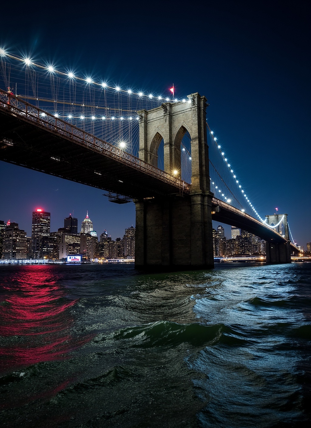 This is a stunning nighttime photograph capturing the Brooklyn Bridge from a vantage point on the water,  likely from a bo...