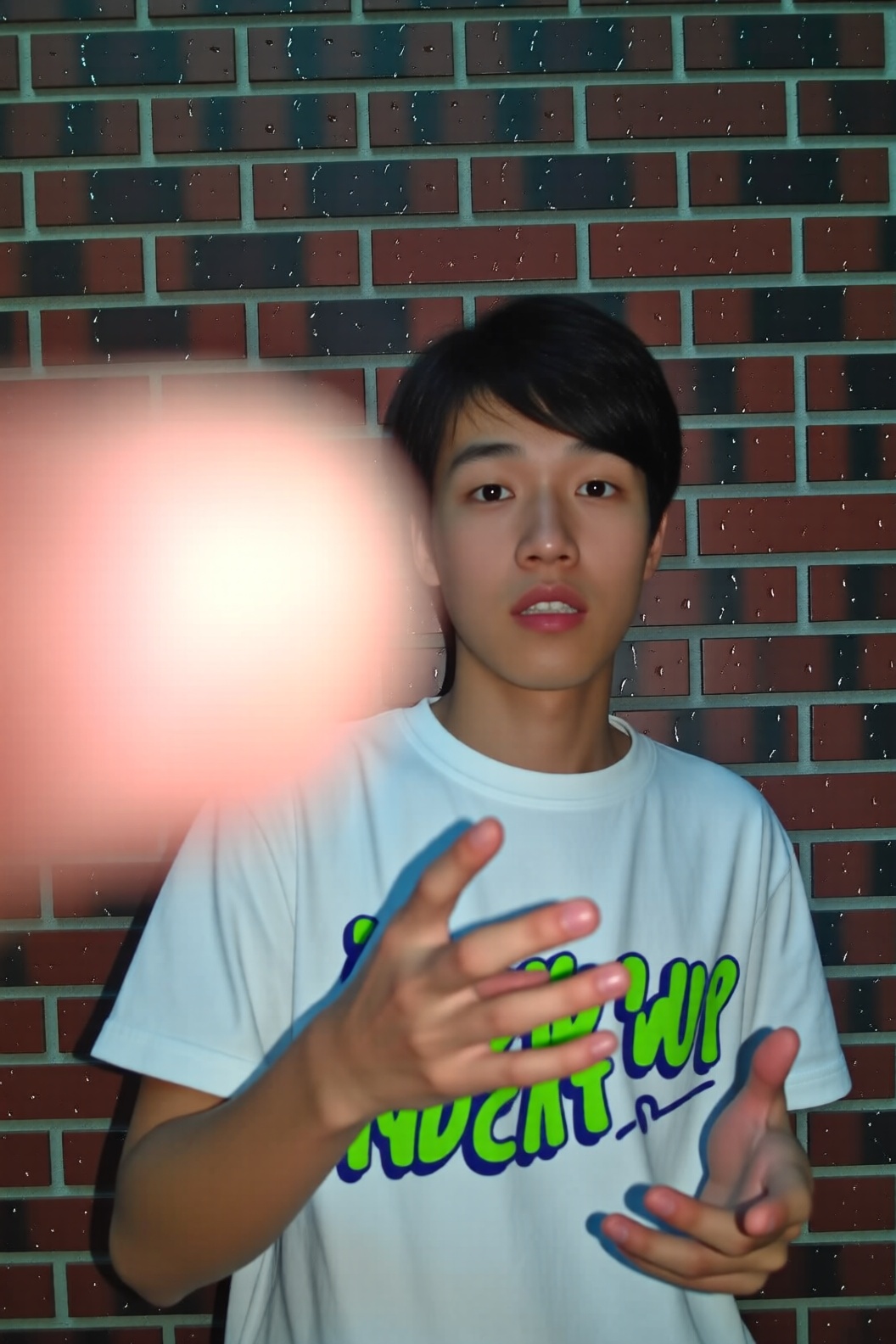 A photo of a young man standing in front of a brick wall,  but the photographer's finger is accidentally covering the left...