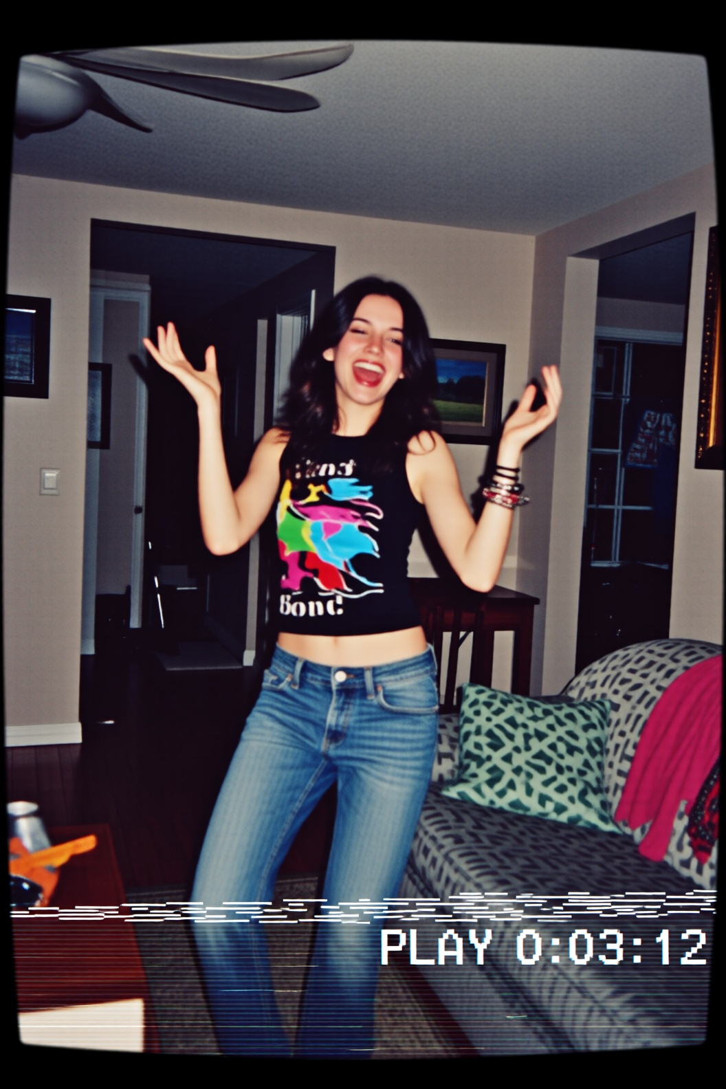 A low-quality VHS screen capture of a young woman standing in the center of a living room,  mid-laugh while attempting a d...