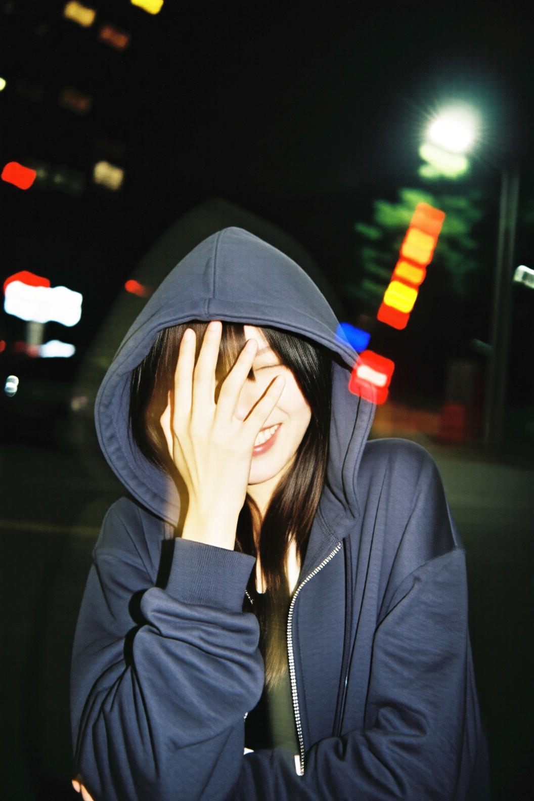A heavily motion-blurred shot of a girl in a hoodie laughing and trying to hide her face with her hand. The shutter speed...