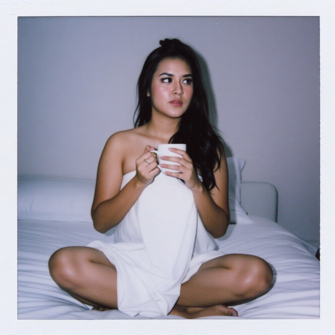 An ******* photo in night time of a young woman named ohwx with wavy black hair sits cross-legged on a white bed,  wrapped...