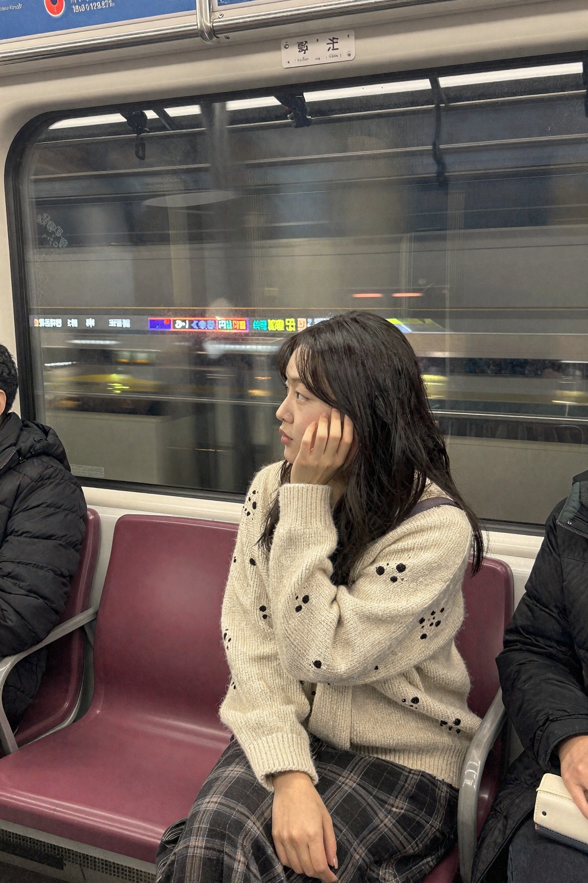 A Korean girl in a cream knit sweater and plaid skirt sitting alone on Seoul subway line 2,  chin resting on her hand,  st...