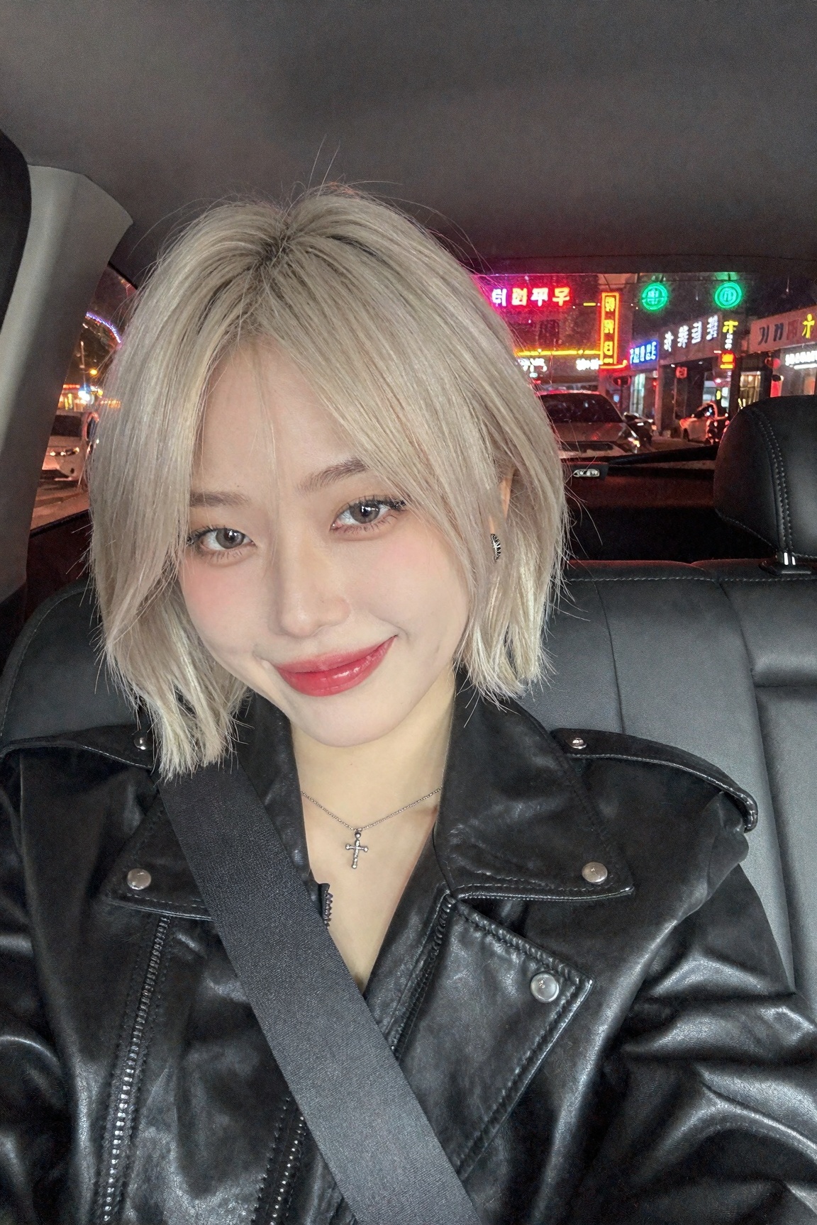 A trendy Hongdae girl with short bleach-blonde wolfcut taking a car selfie at night,  seatbelt across chest,  wearing a bl...