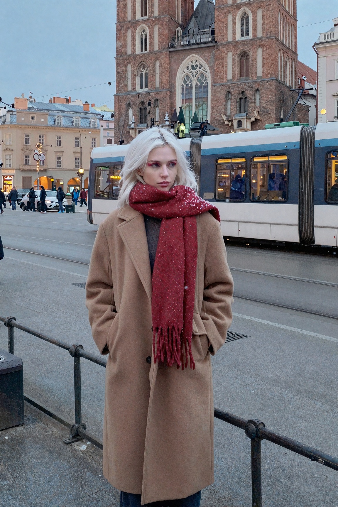 A Polish girl with pale skin and platinum hair waiting for the tram in Kraków old town in winter,  long camel coat and red...