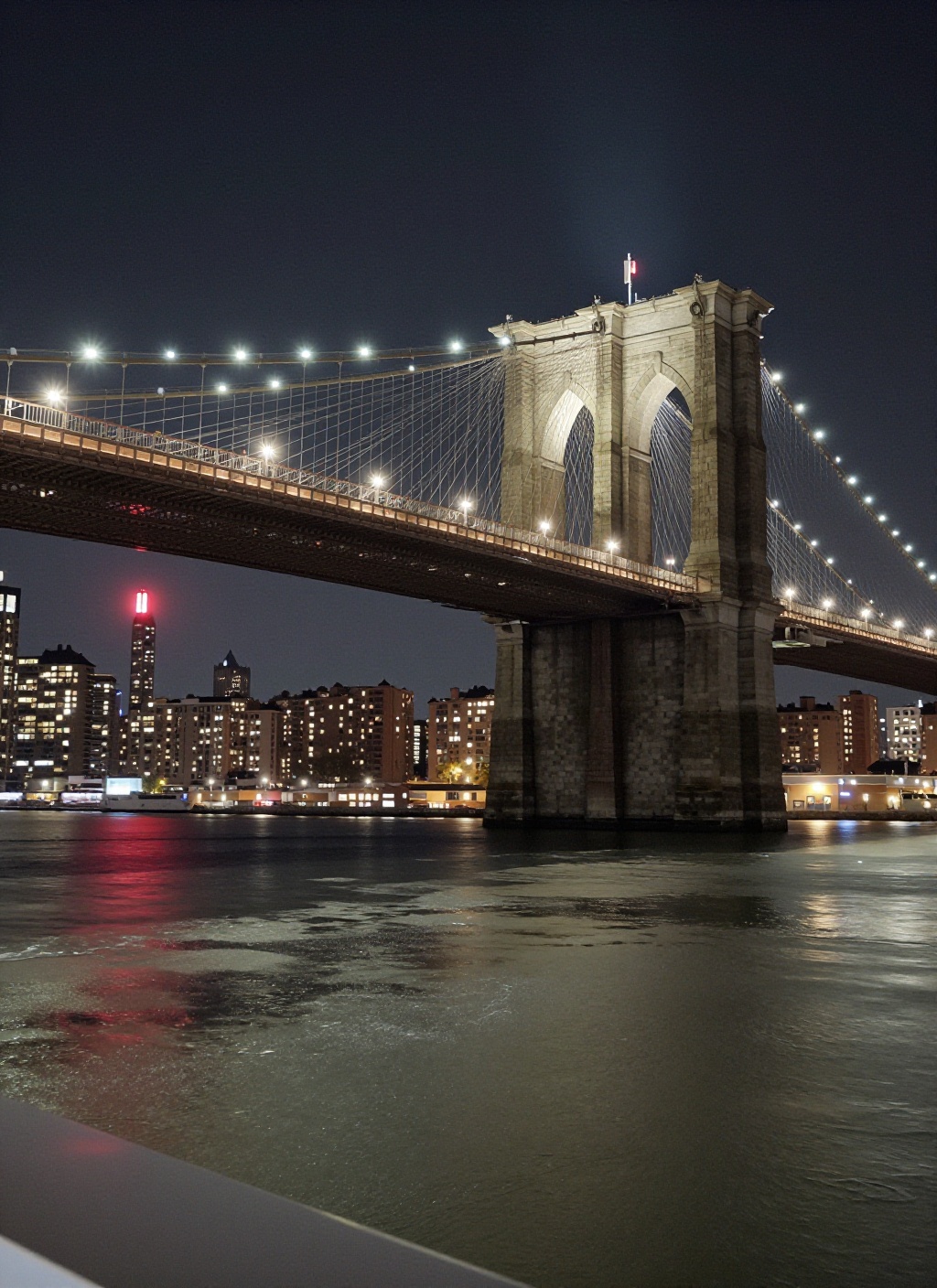 This is a stunning nighttime photograph capturing the Brooklyn Bridge from a vantage point on the water,  likely from a bo...