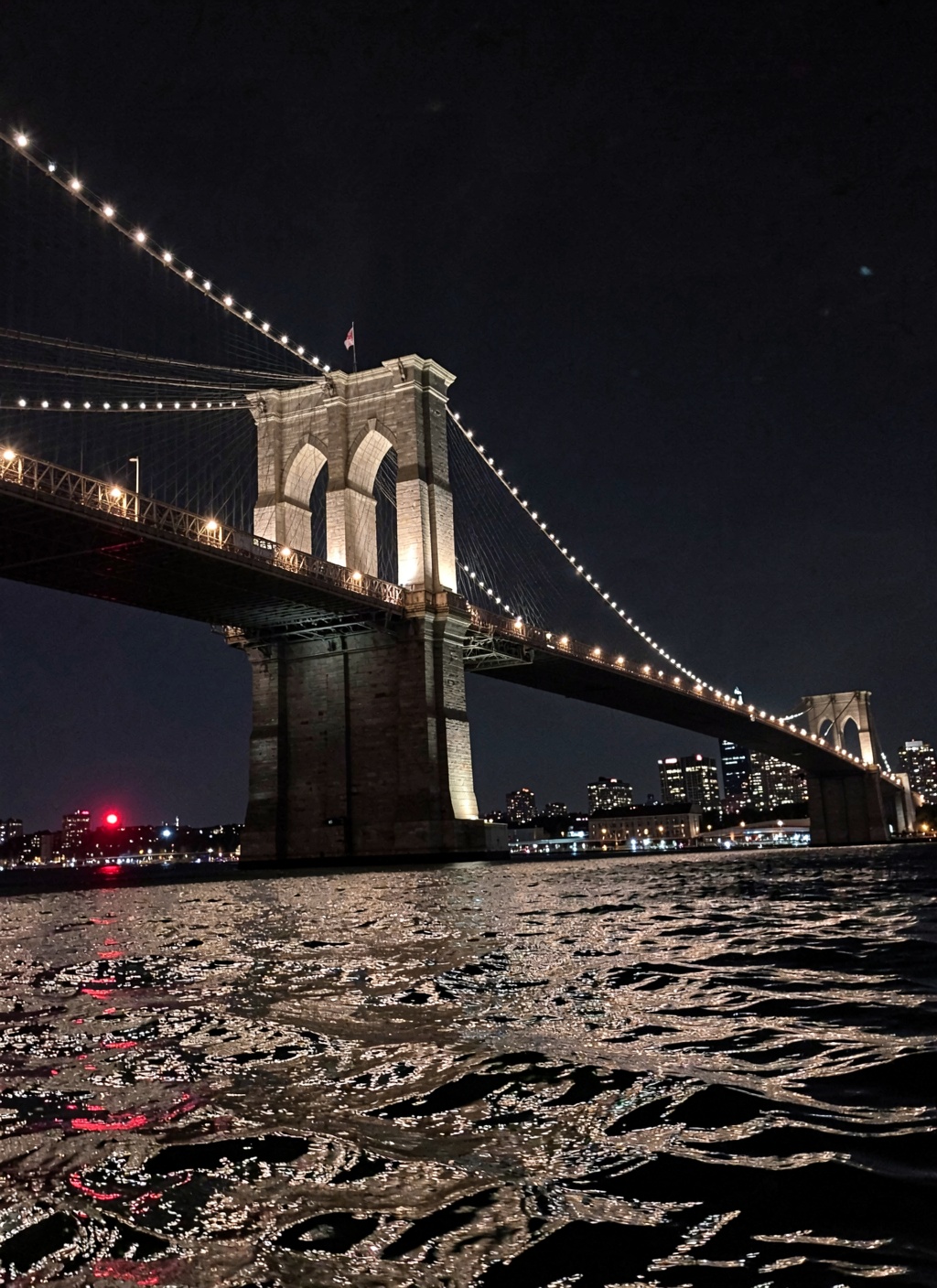 This is a stunning nighttime photograph capturing the Brooklyn Bridge from a vantage point on the water,  likely from a bo...