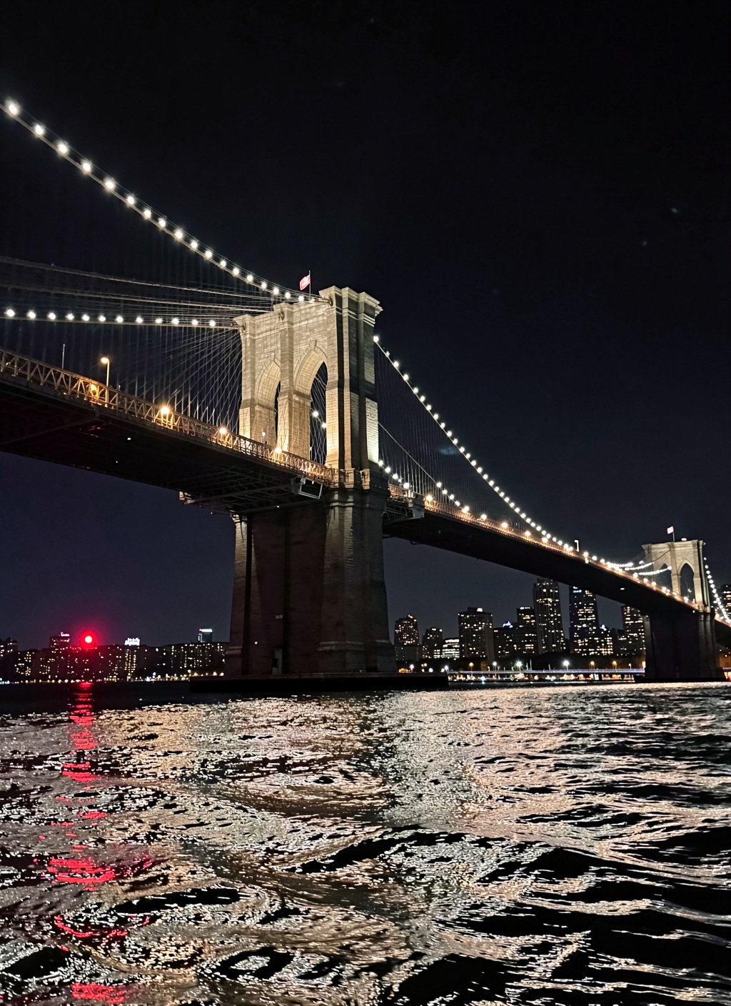 This is a stunning nighttime photograph capturing the Brooklyn Bridge from a vantage point on the water,  likely from a bo...