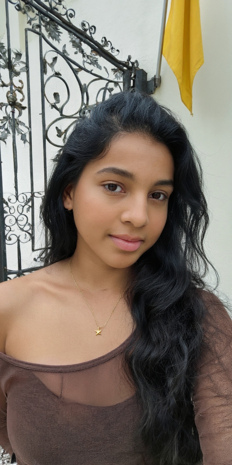 a young woman with long,  wavy black hair and brown eyes,  posing for a selfie in front of a decorative iron gate. she is...