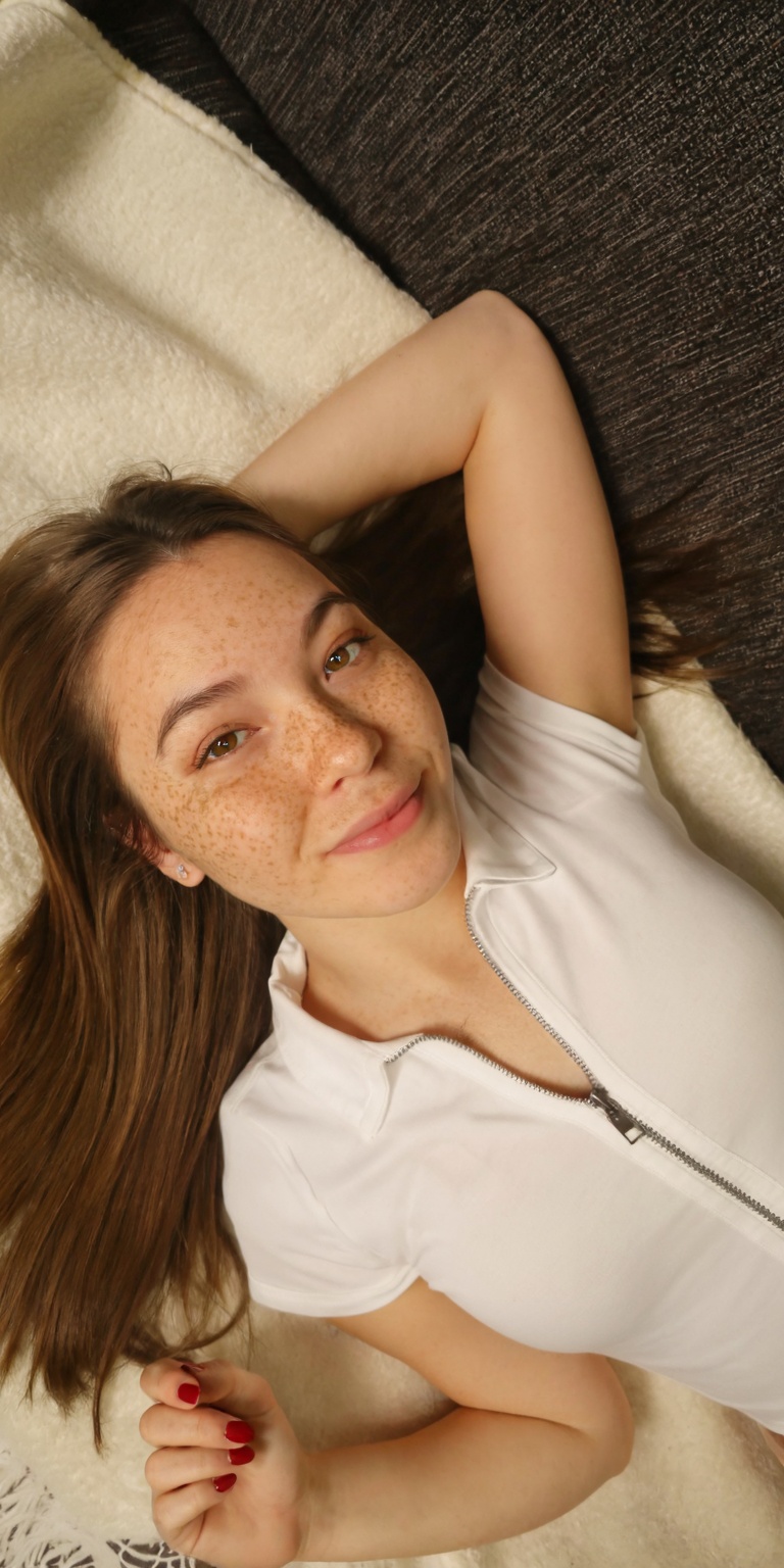 a photo-realistic shoot from above about a young woman with freckles lying on a soft blanket,  looking directly at the cam...