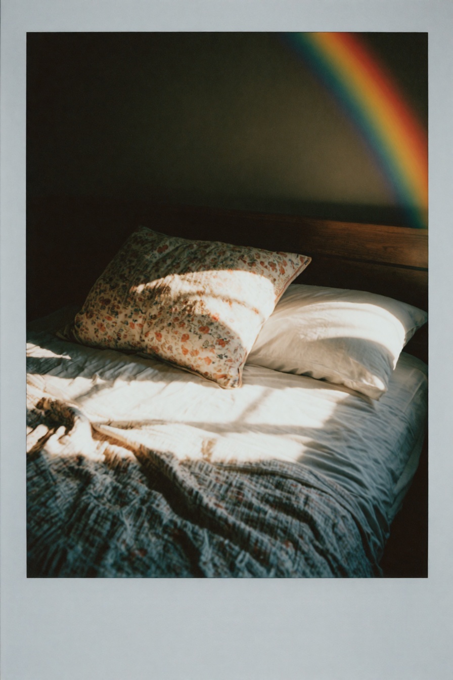 Candid Instax Photo,  The image shows a bed with a white comforter and two pillows on it. The bed is covered in a floral p...
