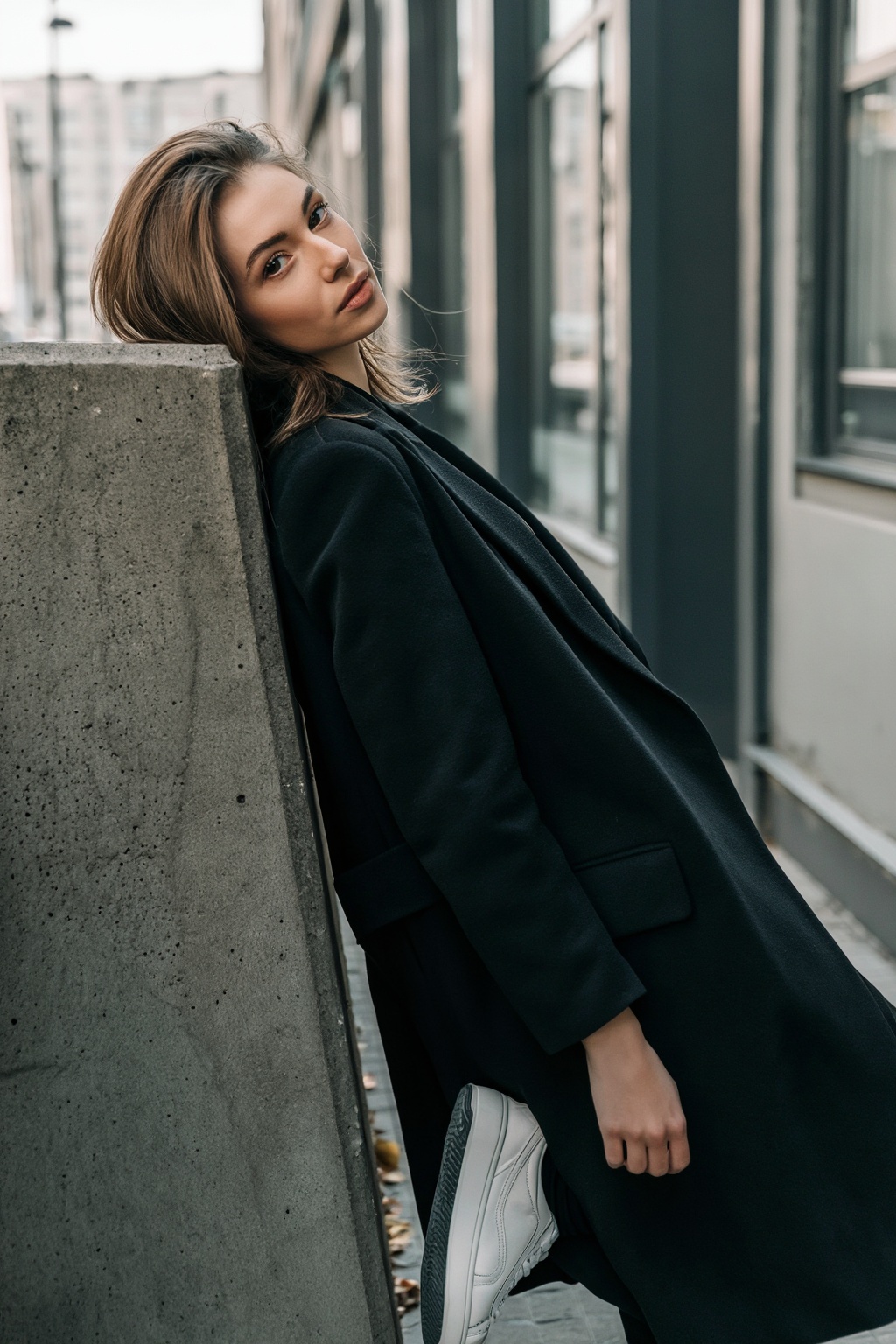 An aesthetic urban portrait of a young woman leaning against a concrete wall in a quiet city street,  photographed in soft...