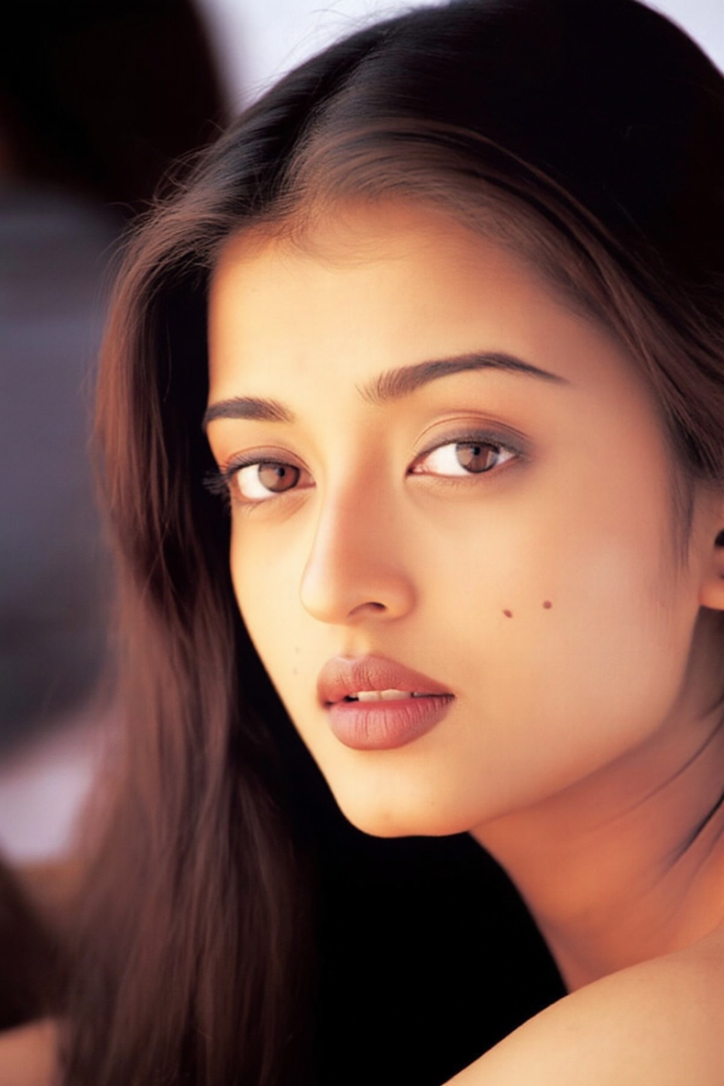 the image features a close-up of a woman with long,  dark brown hair that falls smoothly around her face. Her eyes are a d...