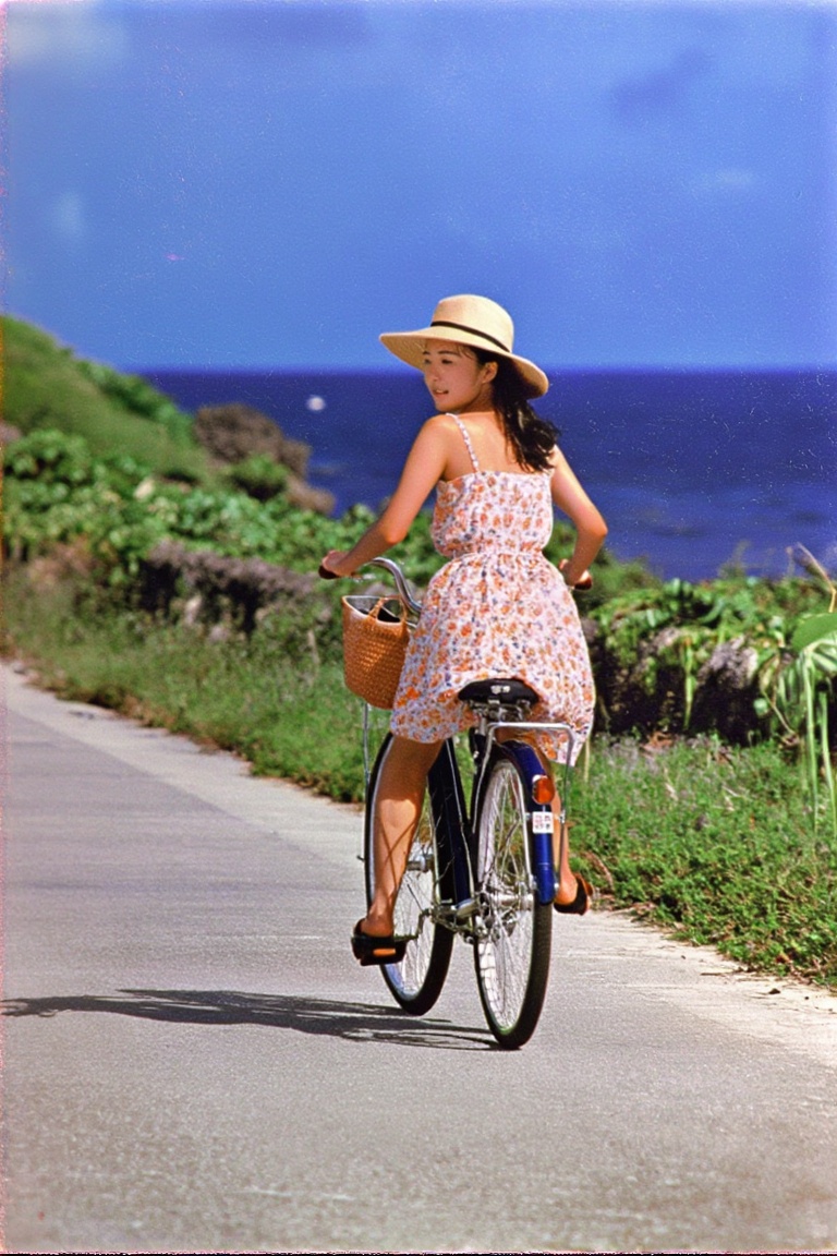 A nostalgic photograph from a photobook. A young woman in a summer dress and a straw hat is riding a bicycle along a seasi...