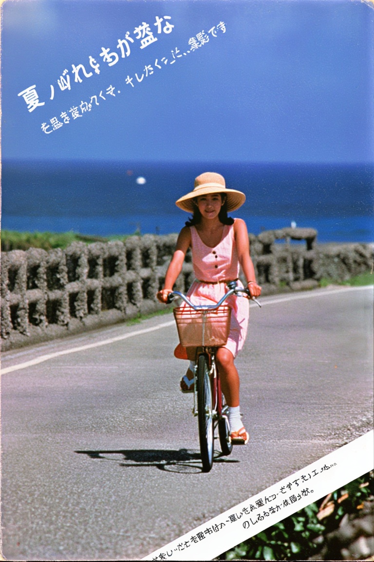 A nostalgic photograph from a photobook. A young woman in a summer dress and a straw hat is riding a bicycle along a seasi...