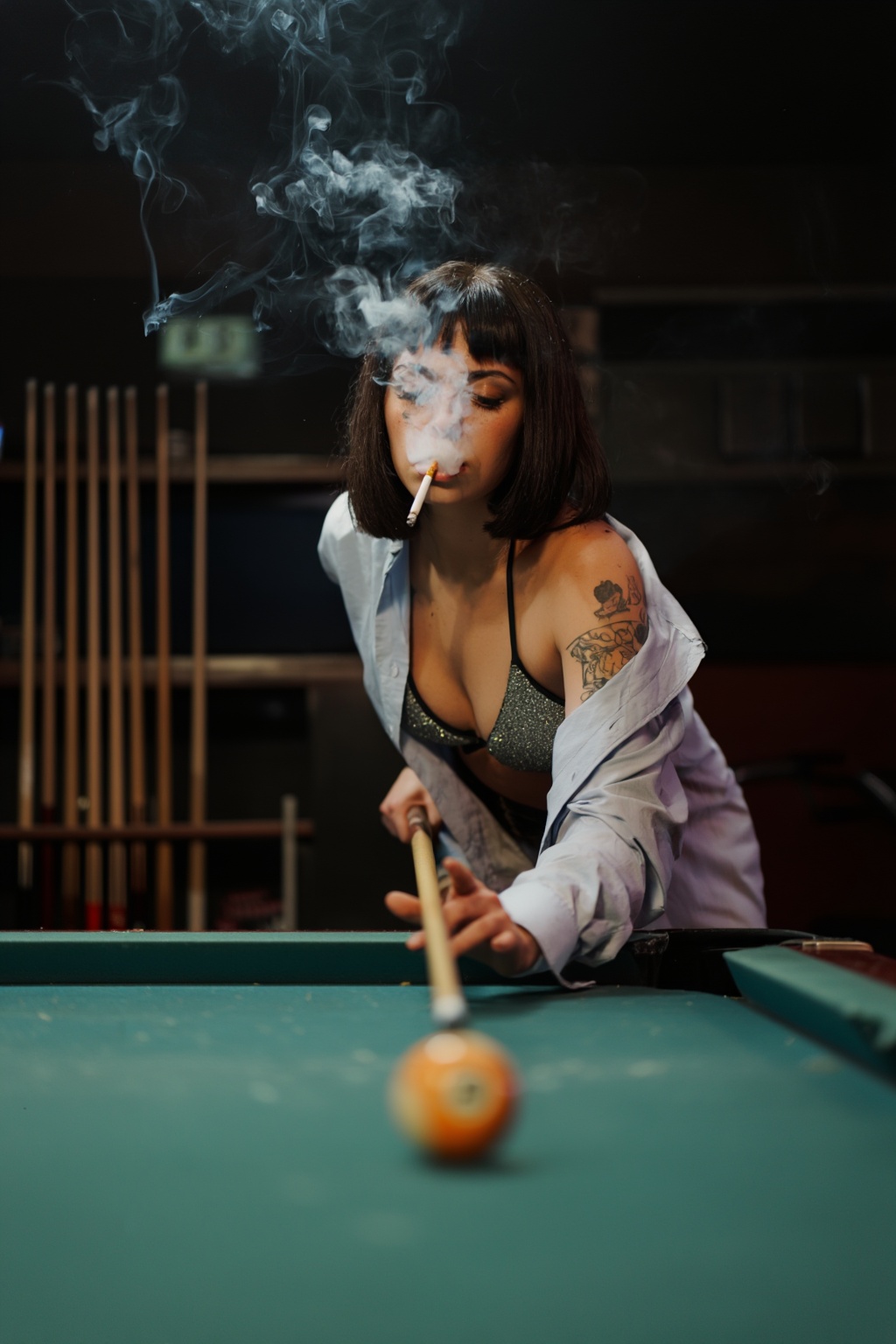 A super moody and cinematic shot of a cool girl with short dark hair and bangs,  leaning low over a pool table in a dimly...