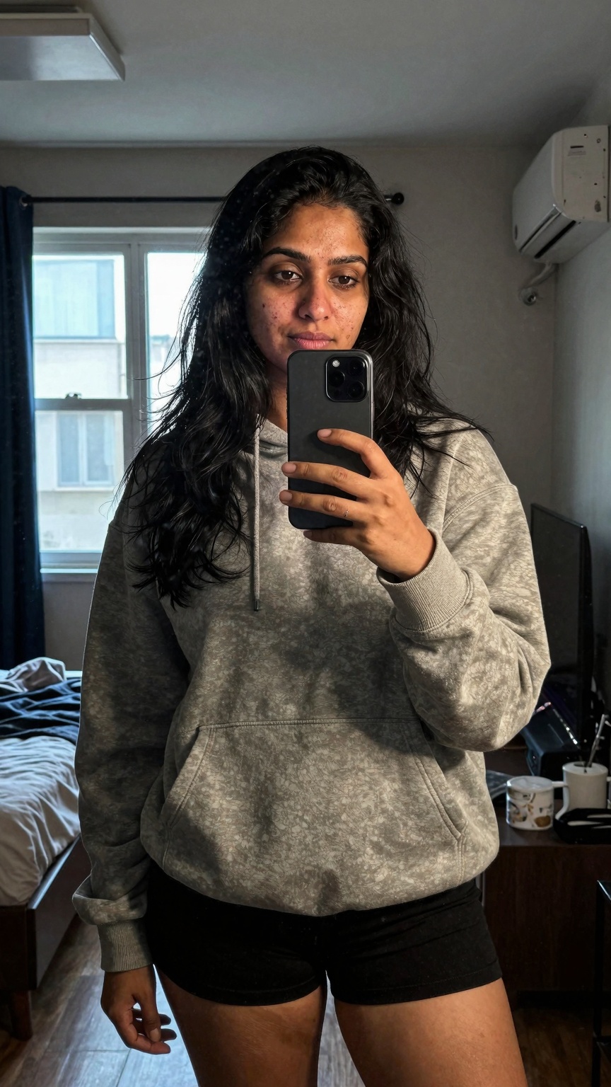 Ultra-realistic mirror selfie mobile photography of a South Asian woman inside a dim apartment bedroom,  shot on Samsung G...