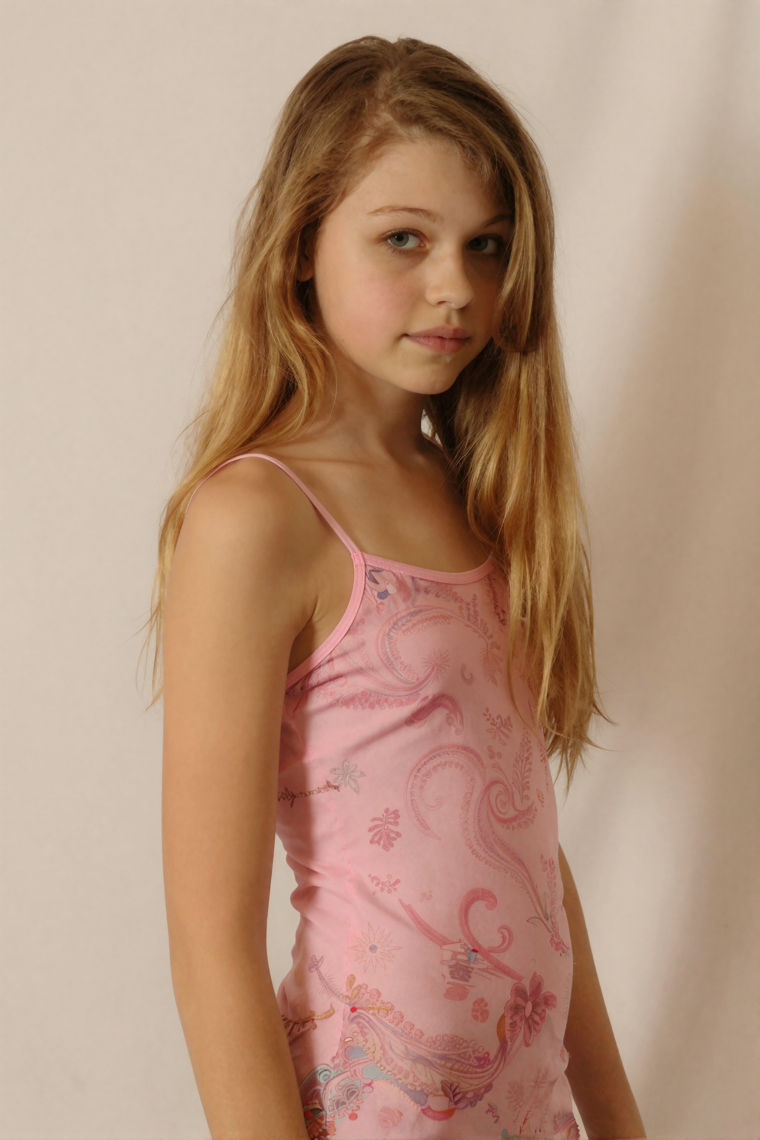 A striking,  intimate photo captures a flat-chested slender blonde 15-year-old girl. Her face is adorned with subtle yet e...