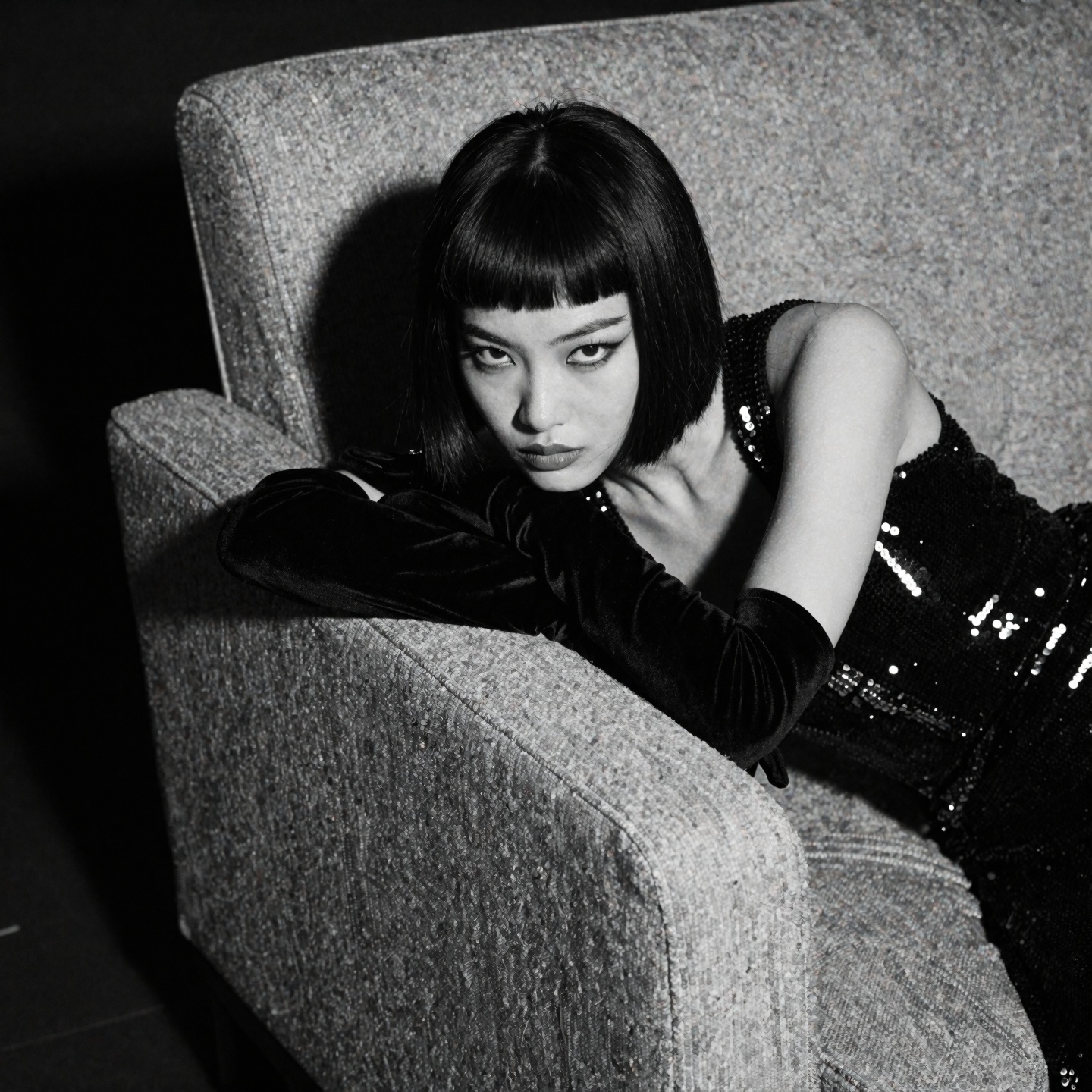 Black-and-white photograph of a young Asian woman with a short,  dark bob and sharp micro-bangs,  her head resting on her...