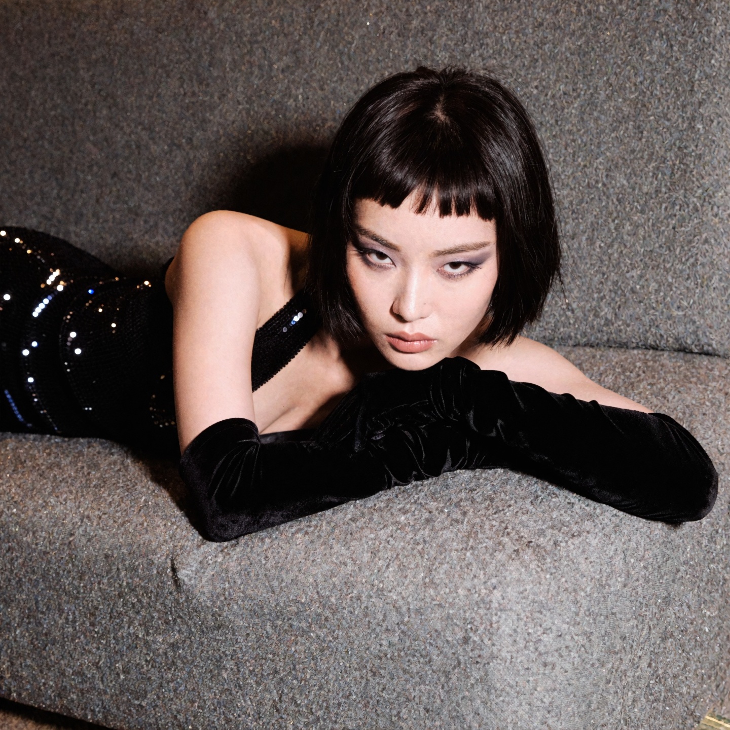 photograph of a young Asian woman with a short,  dark bob and sharp micro-bangs,  her head resting on her folded arms agai...