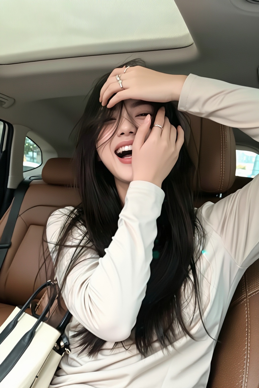 a young woman in a beige long sleeved top is captured in a car,  laughing with her eyes mostly obscured by her hair. her r...