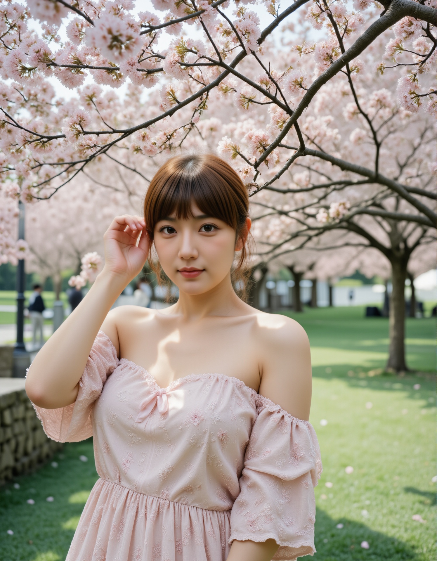 A young woman with long,  straight brown hair and fair skin stands in a park under blooming cherry blossom trees. She is w...
