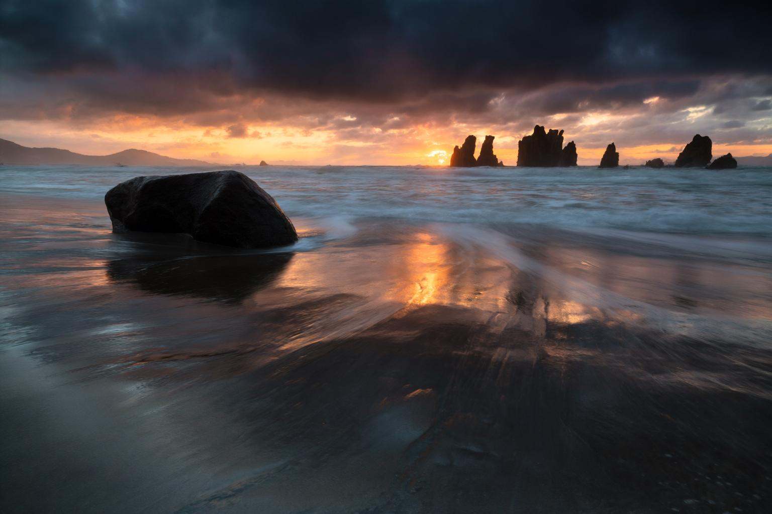 aurelmanea2q photography. A beach scene at sunset. The foreground features a smooth,  wet sand surface with gentle waves l...