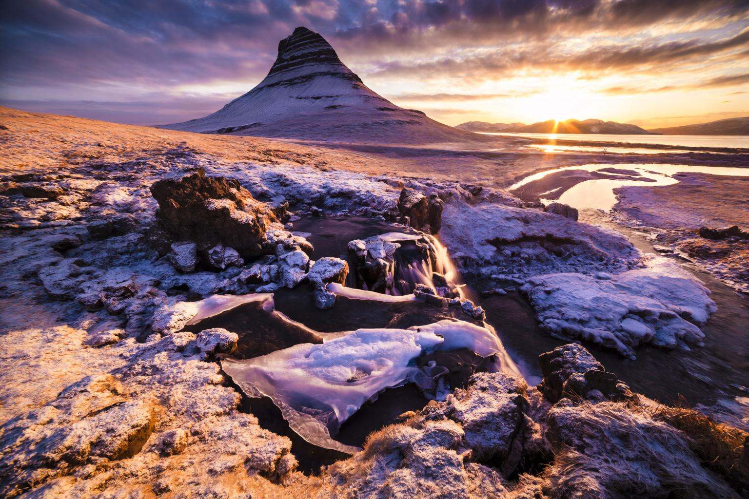 aurelmanea2q photography. A landscape at sunset,  featuring a prominent,  conical mountain in the foreground. The mountain...