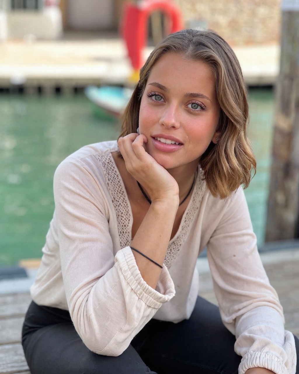 margarida_corceiro,  likely in her early twenties,  seated on a wooden deck overlooking a serene canal. She has a light ol...