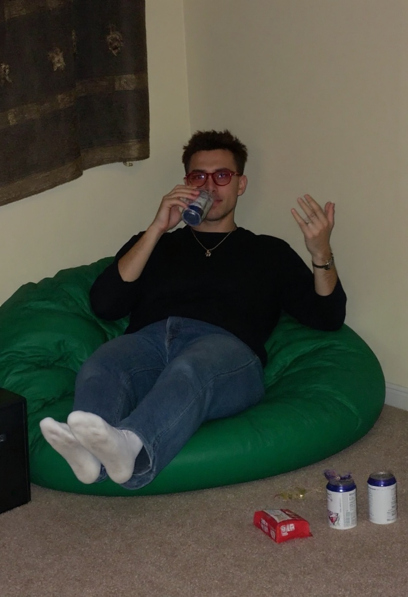 This photograph captures A male friend sitting back on a green bean bag,  drink in hand and socks off,  with red-tinted gl...