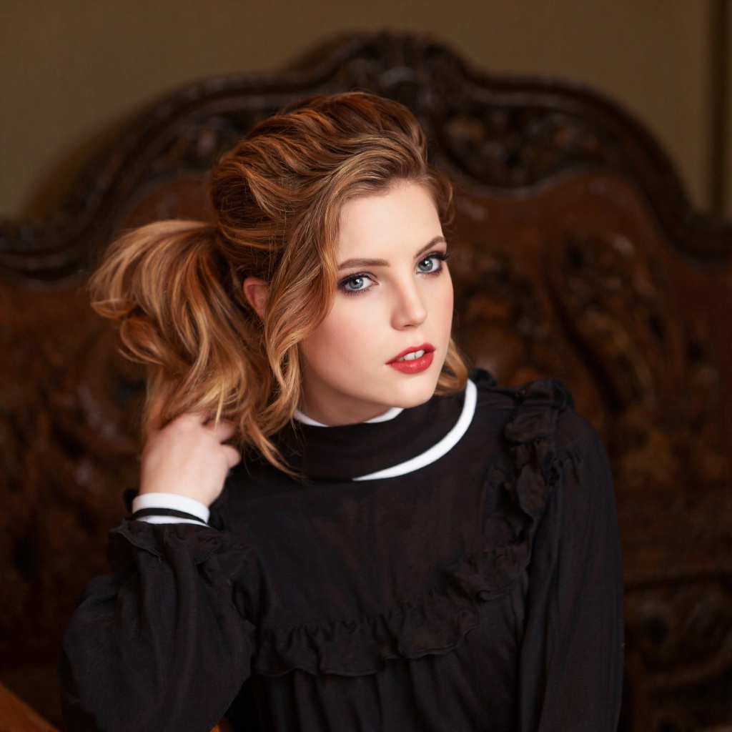 A portrait of sydney_sierota in a vintage setting. She wears a dark,  ruffled blouse with a white collar. Her hair is styl...