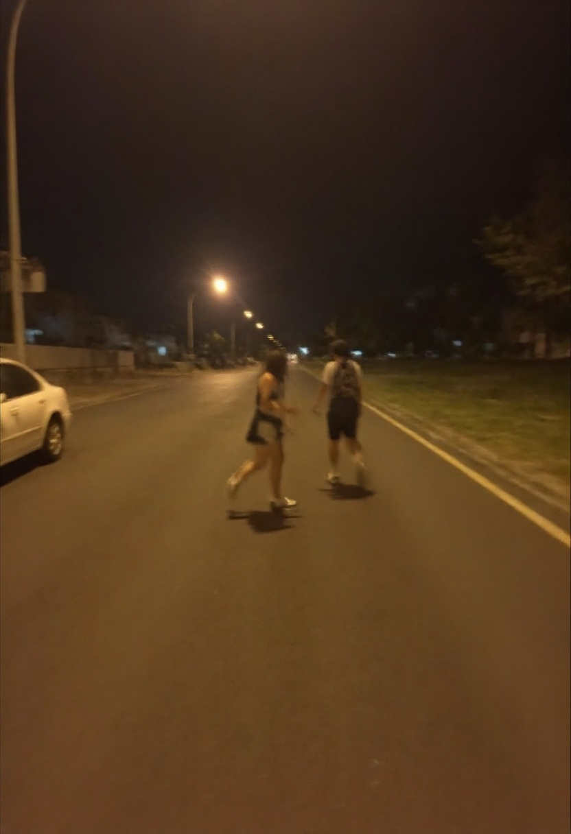 This photograph captures a nighttime scene on an urban street. The image is taken from a slightly low angle,  with a dim,...