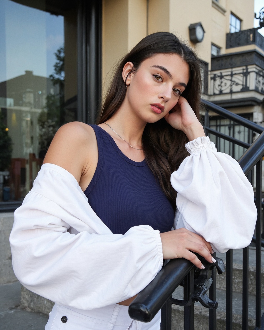 deva_cassel leaning against a metal railing on an outdoor staircase,  set against a modern urban backdrop. She has long,...