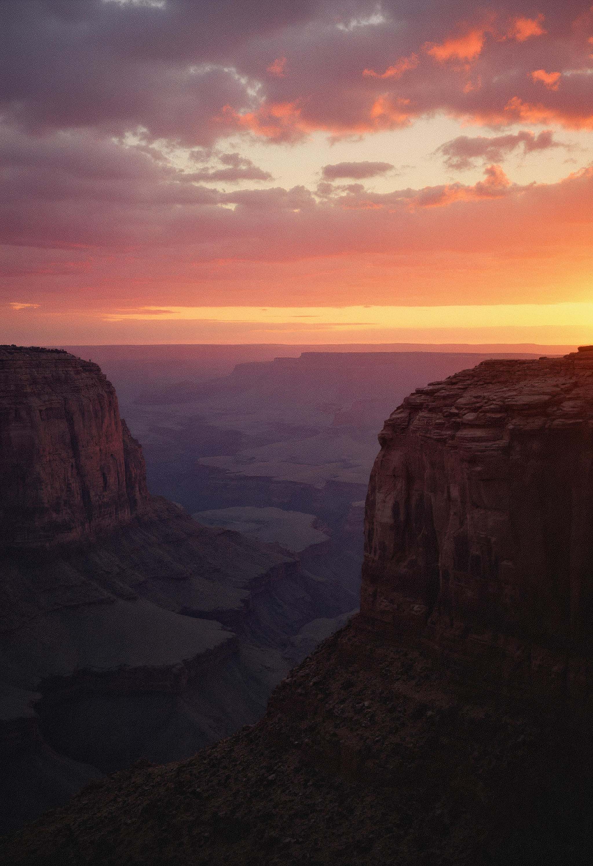 A wide landscape shot of a canyon,  side-lit by the setting sun,  casting dramatic shadows and highlighting the rugged tex...
