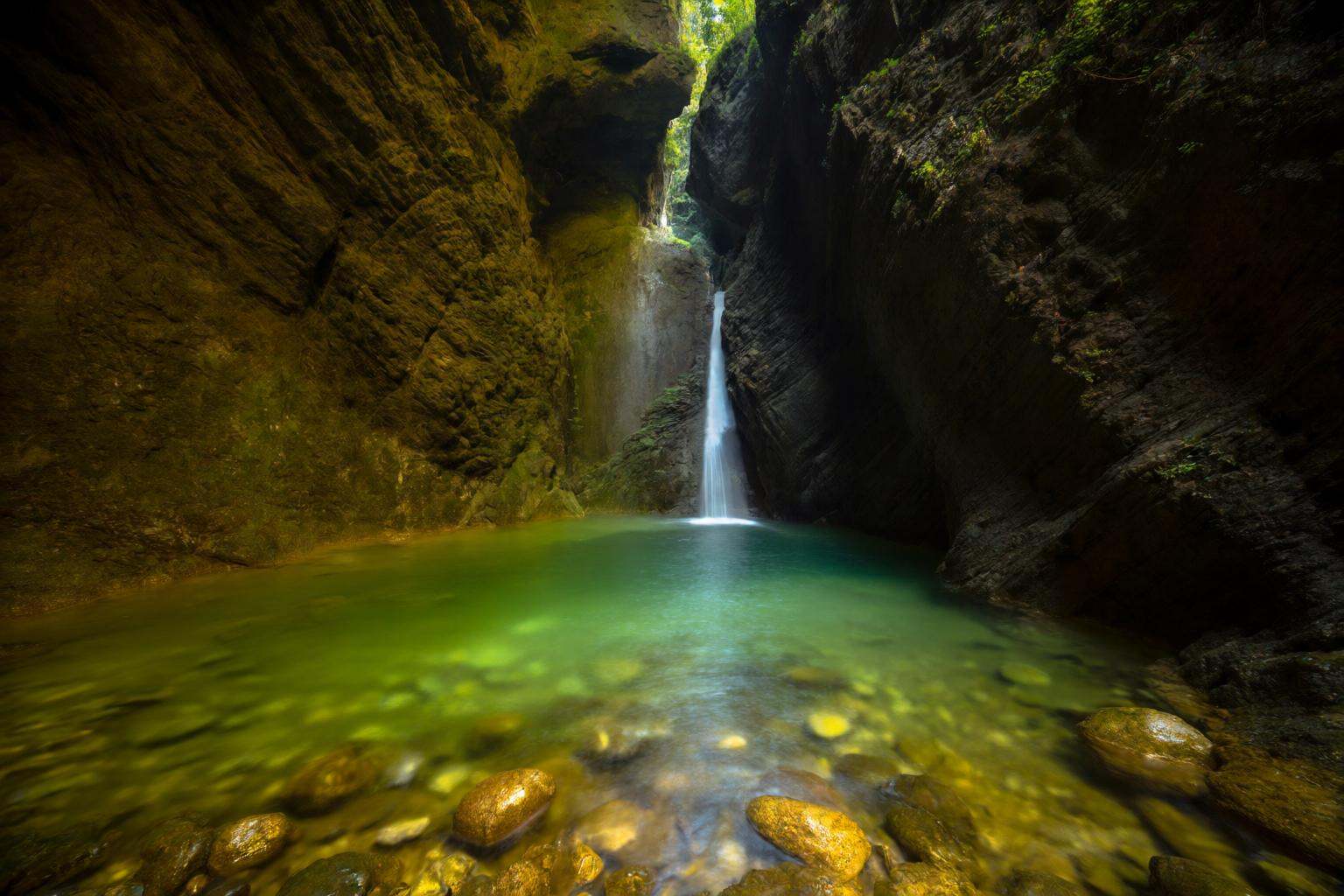 aurelmanea2q photography. A scene of a narrow canyon with towering rock walls on either side. At the center of the image,...