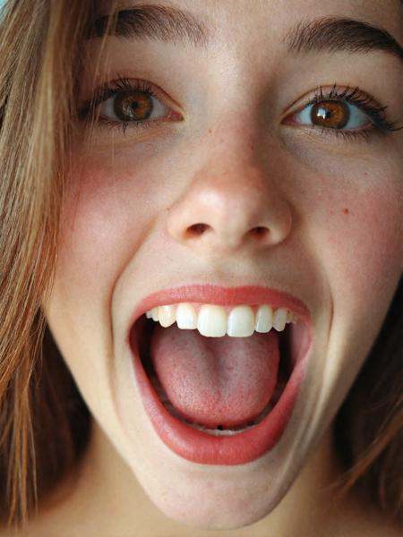 A photograph of a young [*******|student] woman's face with brown eyes,  long hair,  and her mouth wide open. The focus is...