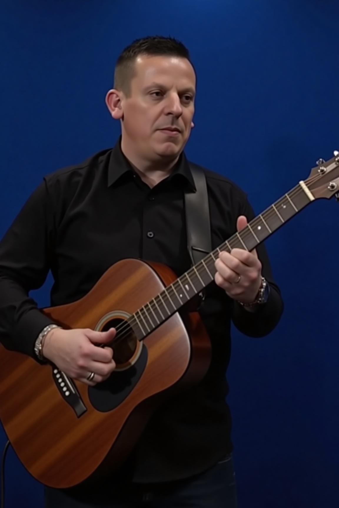 A high-resolution photograph of Dave Chisnall playing an acoustic guitar against a solid,  deep blue background. The man,...