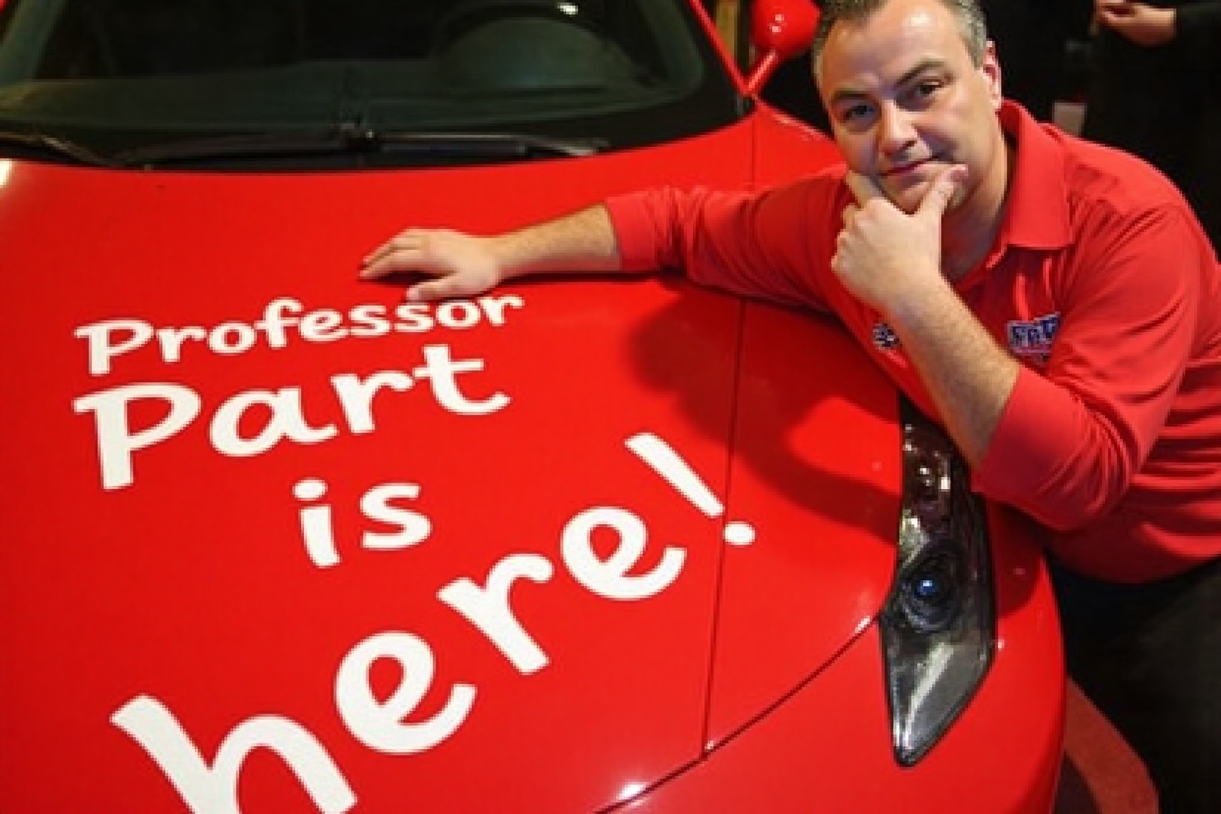 A high-resolution photograph of John Part laying on the hood of a ferrari with his head resting on his hand. Text reading...
