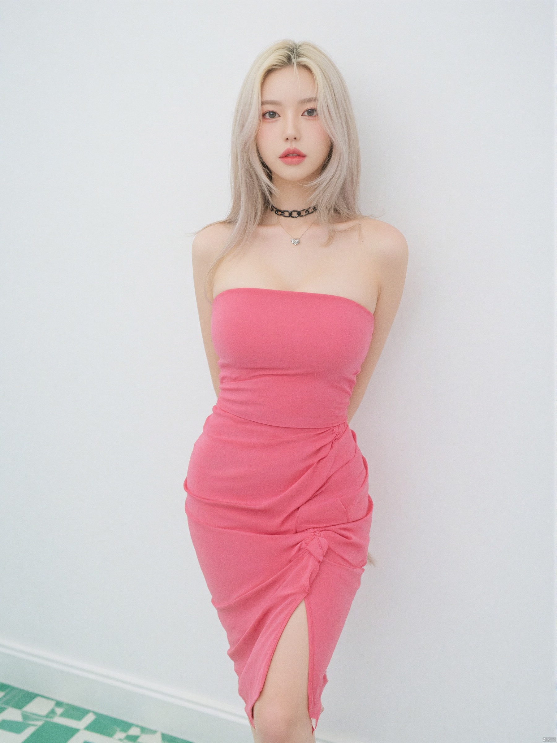 a woman in a pink strapless dress stands in front of a white wall. The woman's dress is adorned with a black chain around her neck, The backdrop is a stark white, with a green checkerboard pattern on the floor, creating a stark contrast to the woman's outfit.